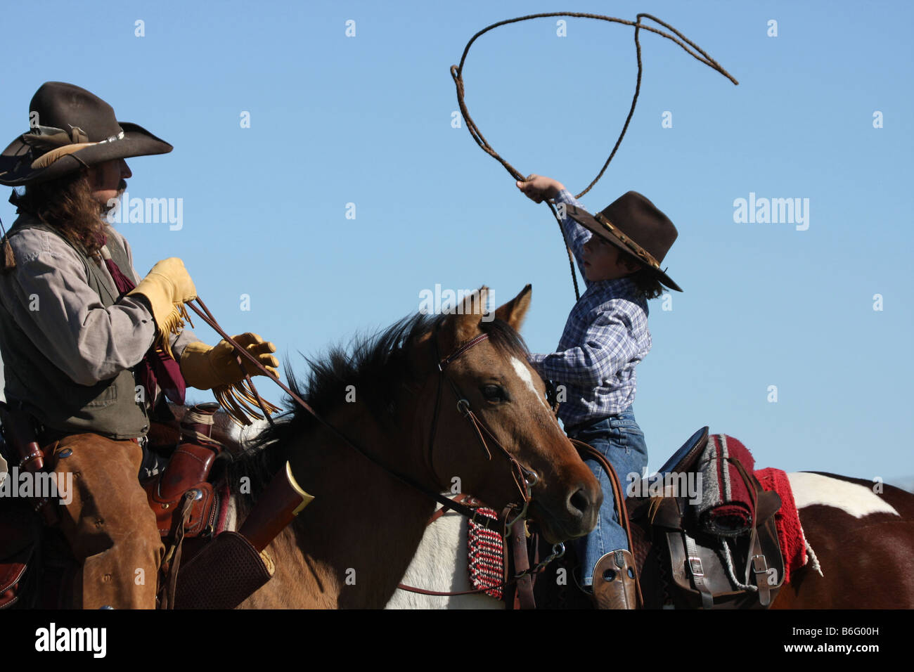 A cowboy father on horseback showing his son how to throw a rope to