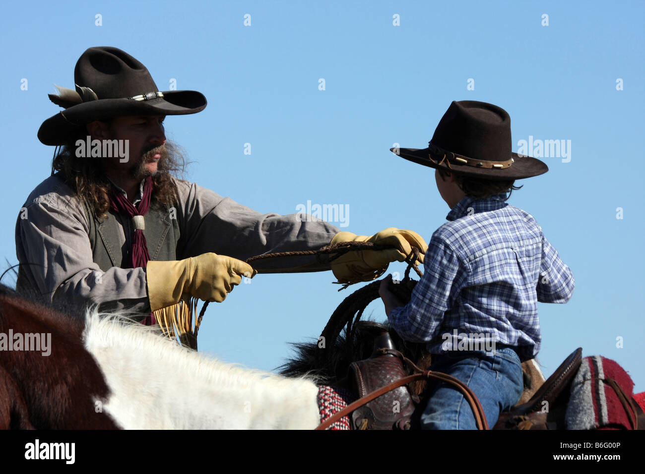 A cowboy on horseback showing his son how to throw a rope to catch