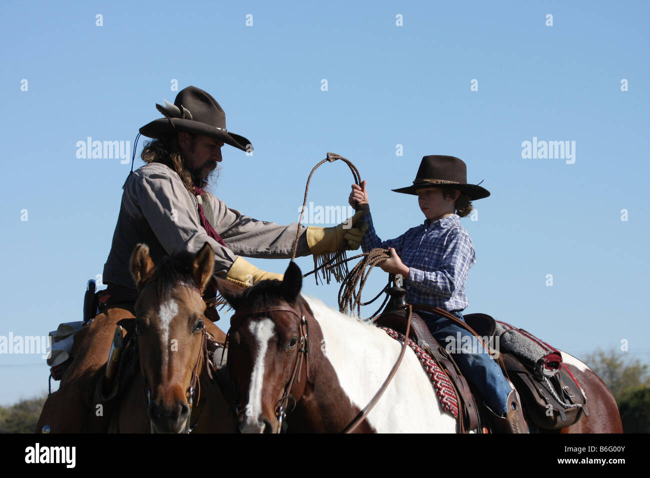 A cowboy father on horseback showing his son how to throw a rope to