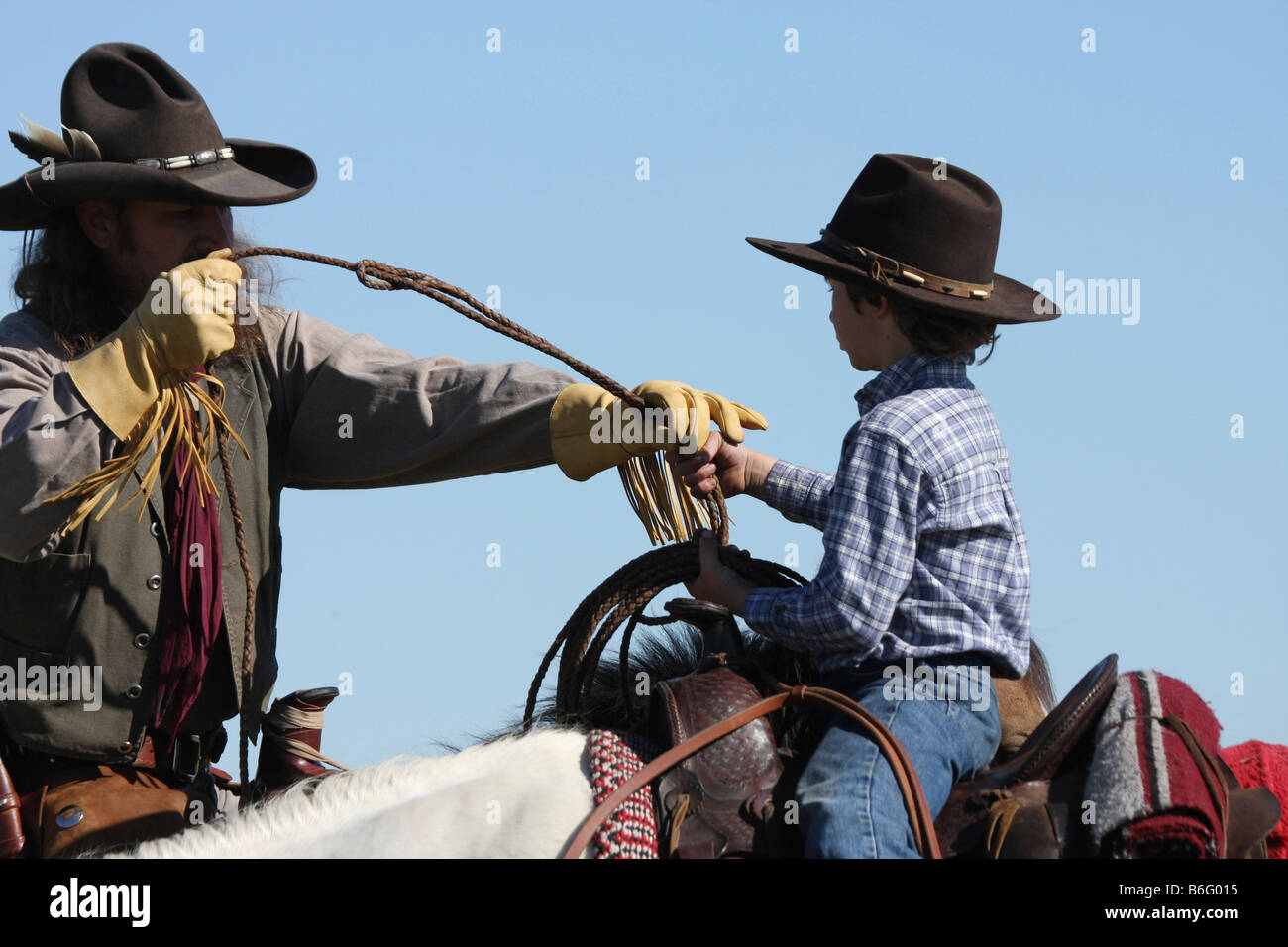 A cowboy father on horseback showing his son how to throw a rope to