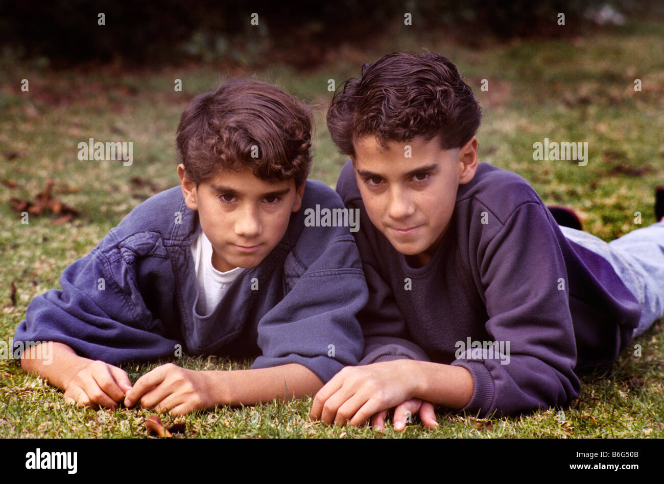 Twin boys relax on grass in yard of home. Stock Photo