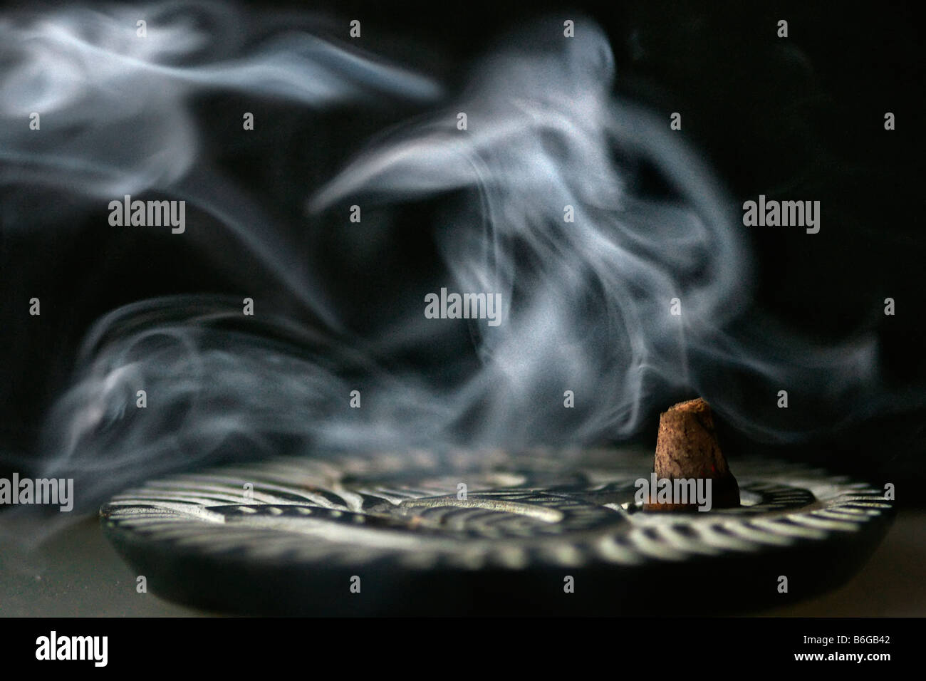 Tranquil incense plume salvia smudge abstraction burning on small plate on black background smoke resembling sea horse shape Stock Photo