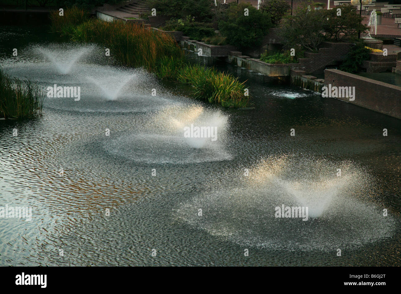 Light from the setting sun catches the fouintain jets in an aerial view of the Lakeside Public gardens at the Barbican Centre Stock Photo