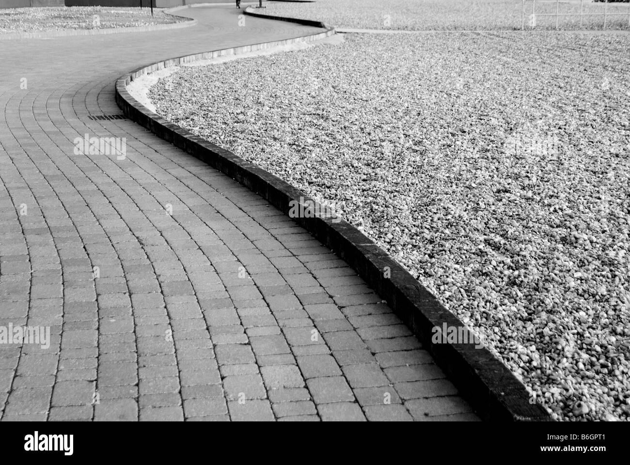 A curved brick pathway with a wooden boarder stopping the pebbles from Brighton beach getting on the walk way Stock Photo