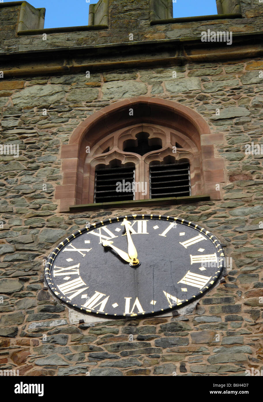 Stone church clock tower with metal clock face showing 11.59, stone mullion window above and castellations Stock Photo
