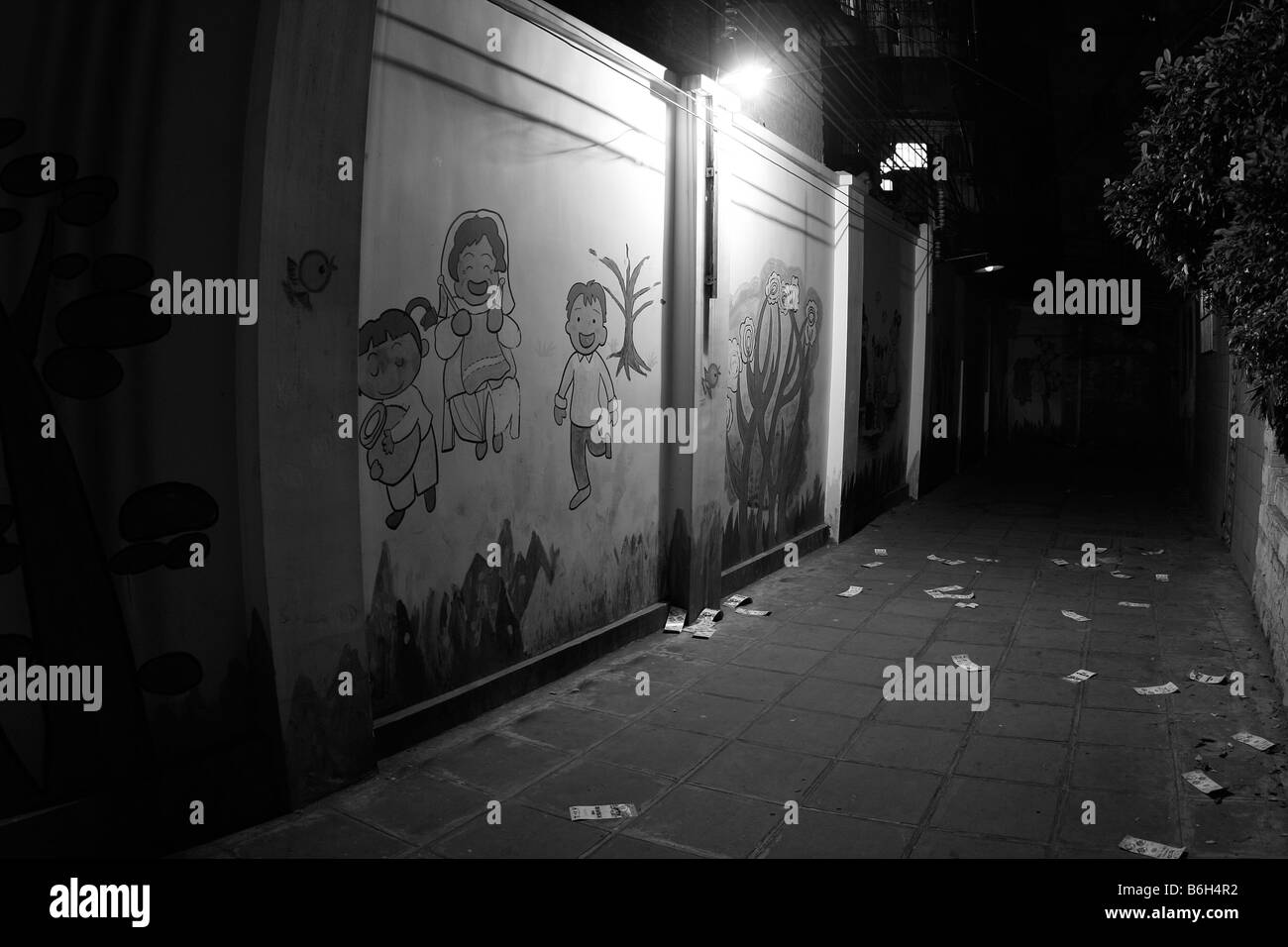 Lonely old darkly lit corner alley past an old warehouse in the shadows of overhead streetlights in China near painted walll Stock Photo