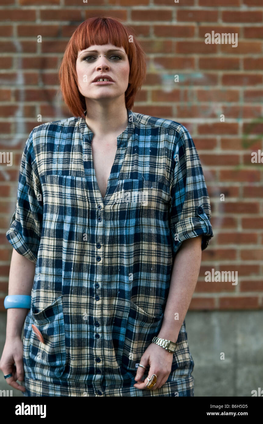 fiery red haired young  woman girl looking angry furious full of rage and hatred in a run down area of a town or city Stock Photo