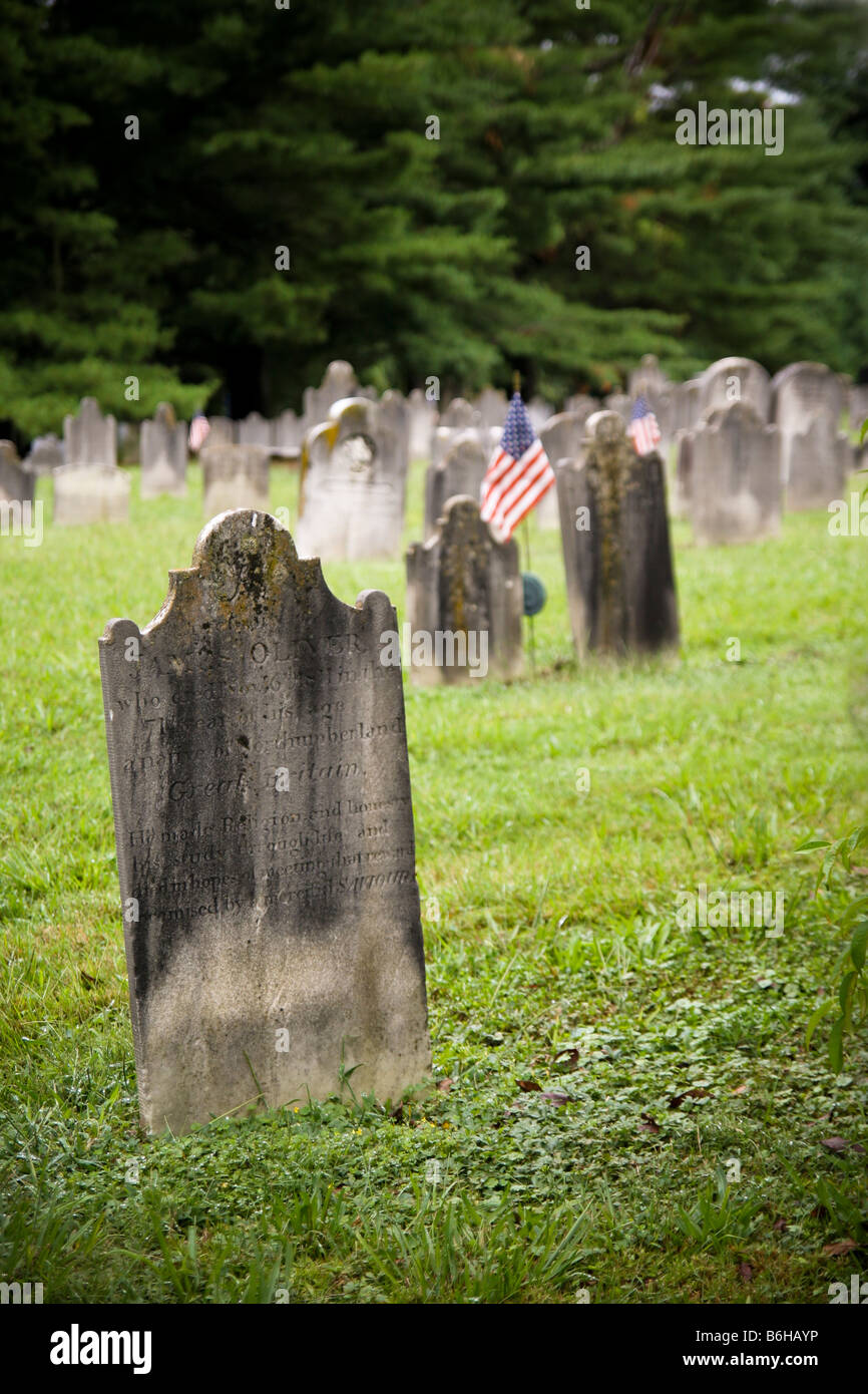 Old American cemetery with both 18th and 19th century era tombstones, an American flag marks a veterans grave in the background. Stock Photo