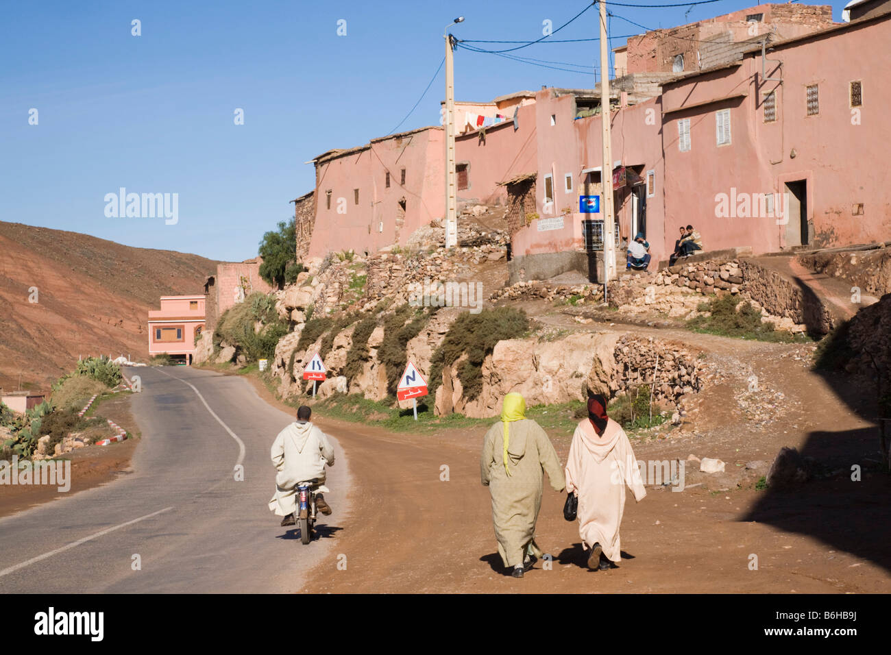 Typical Berber mountain village scene with two traditionally dressed women walking beside road. Tahanaoute Asni Valley Morocco Stock Photo