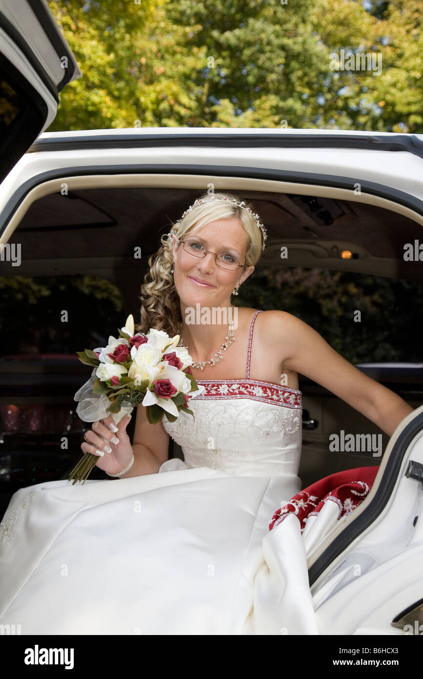 Blushing blonde bride prepares to step out of white wedding car Stock