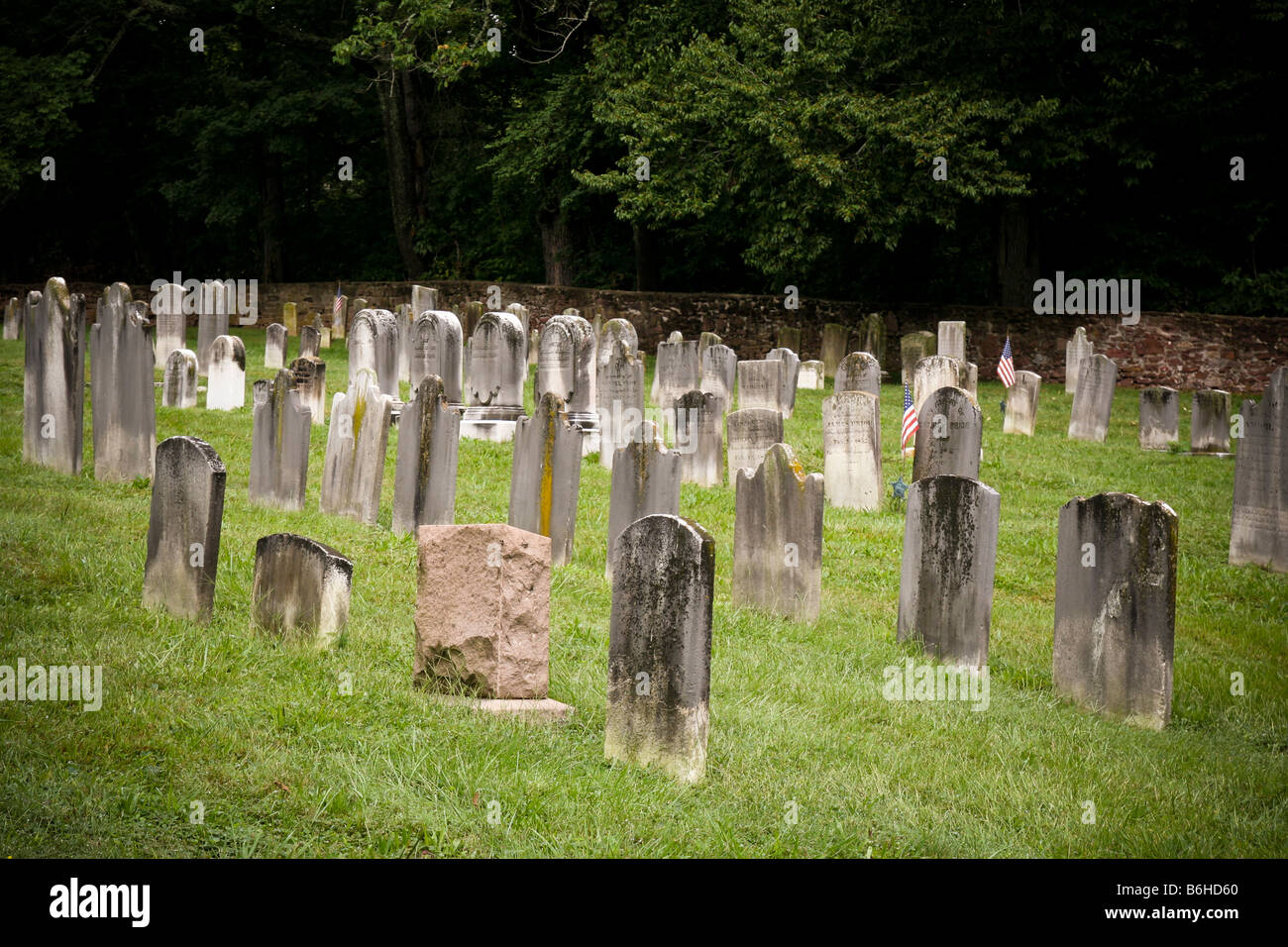 A old early American church grave yard with rows of simple marble grave markers, a stone wall and trees in the background. Stock Photo