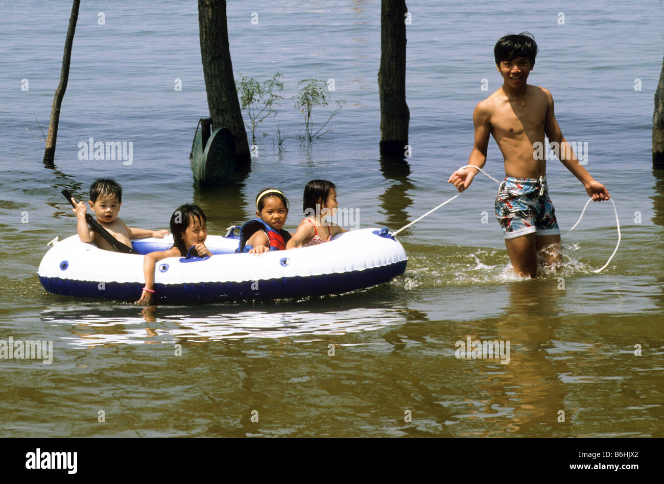 Asian man pulls inflated raft full of children in lake. Stock Photo