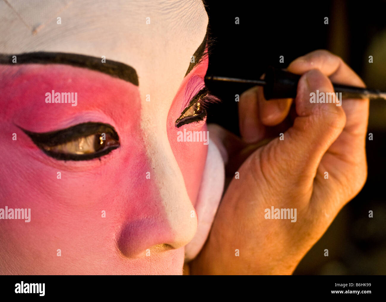 An actress makes-up herself during a chinese opera rehearsal. In this caption, she is carefully painting her eyes. Stock Photo