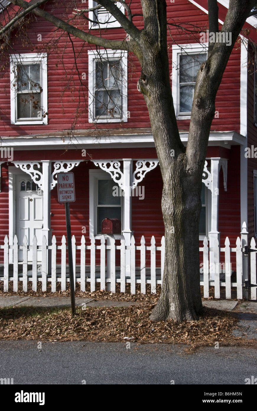 red-painted Victorian house housefront with white trim, fretwork detailing on front porch post brackets & white picket fence Stock Photo