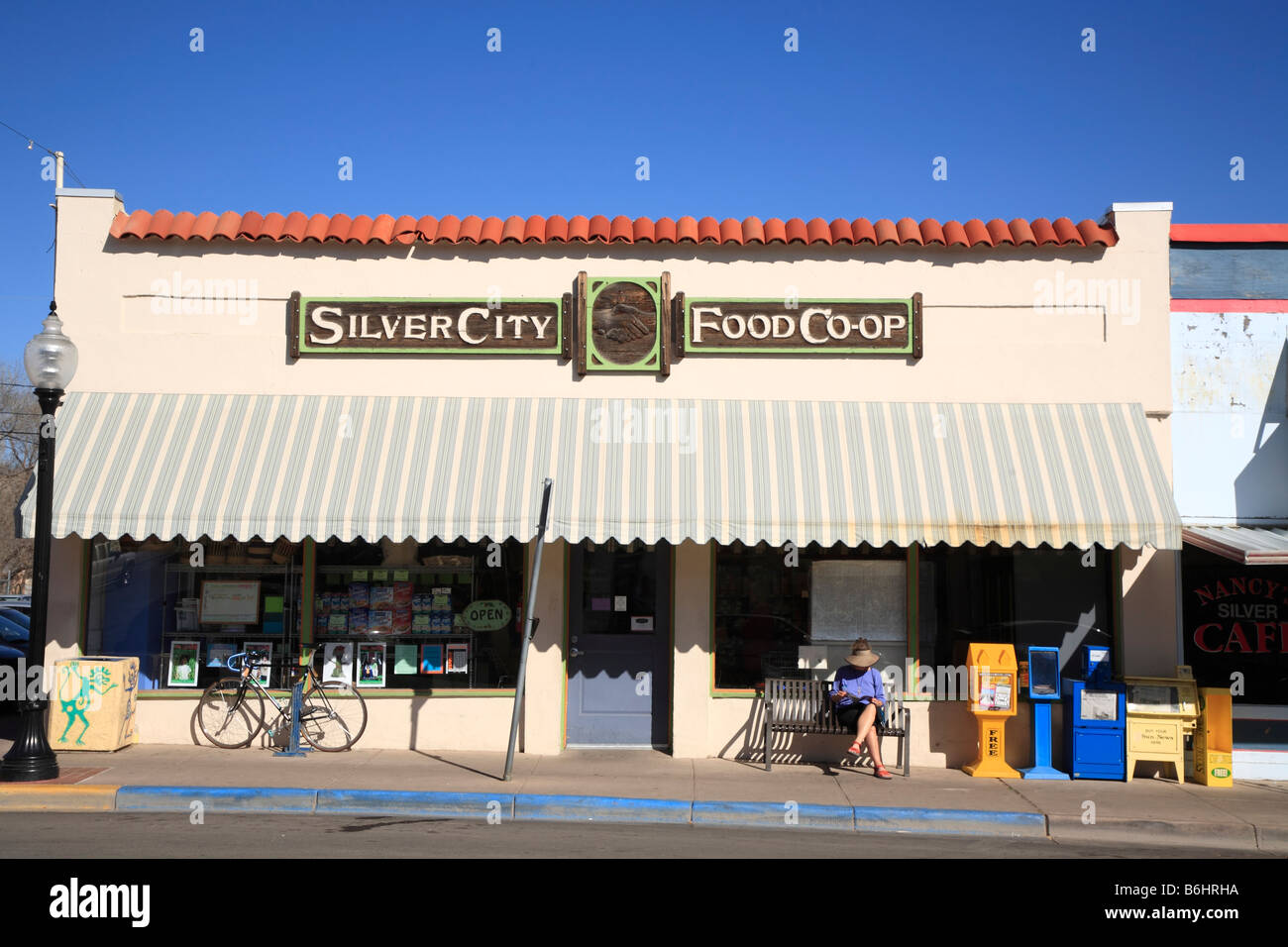 Person sitting on a bench outside a quaint co-op natural food store downtown Bullard St Silver City, New Mexico, United States Stock Photo