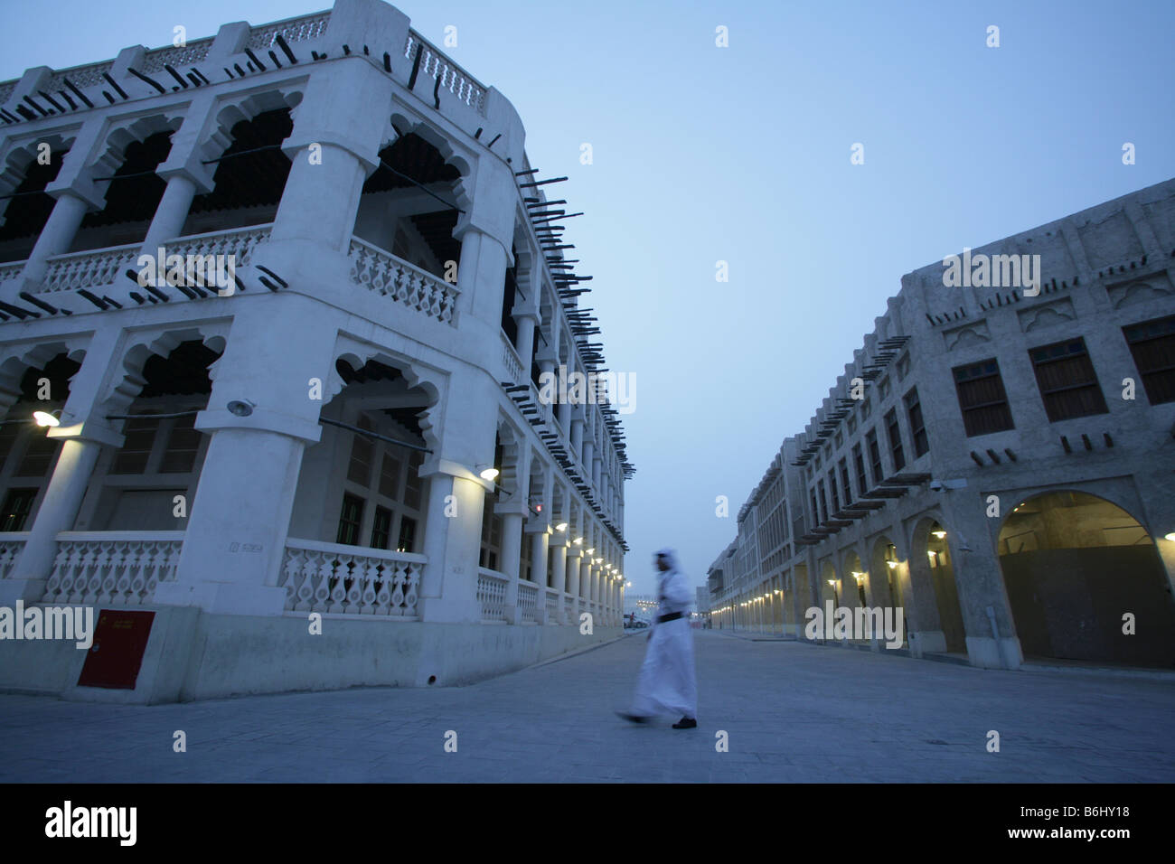 Man walking past traditional whitewash buildings at Souq Waqif market with protruding 'shandal' beams at dusk, Doha, Qatar, Middle East Stock Photo