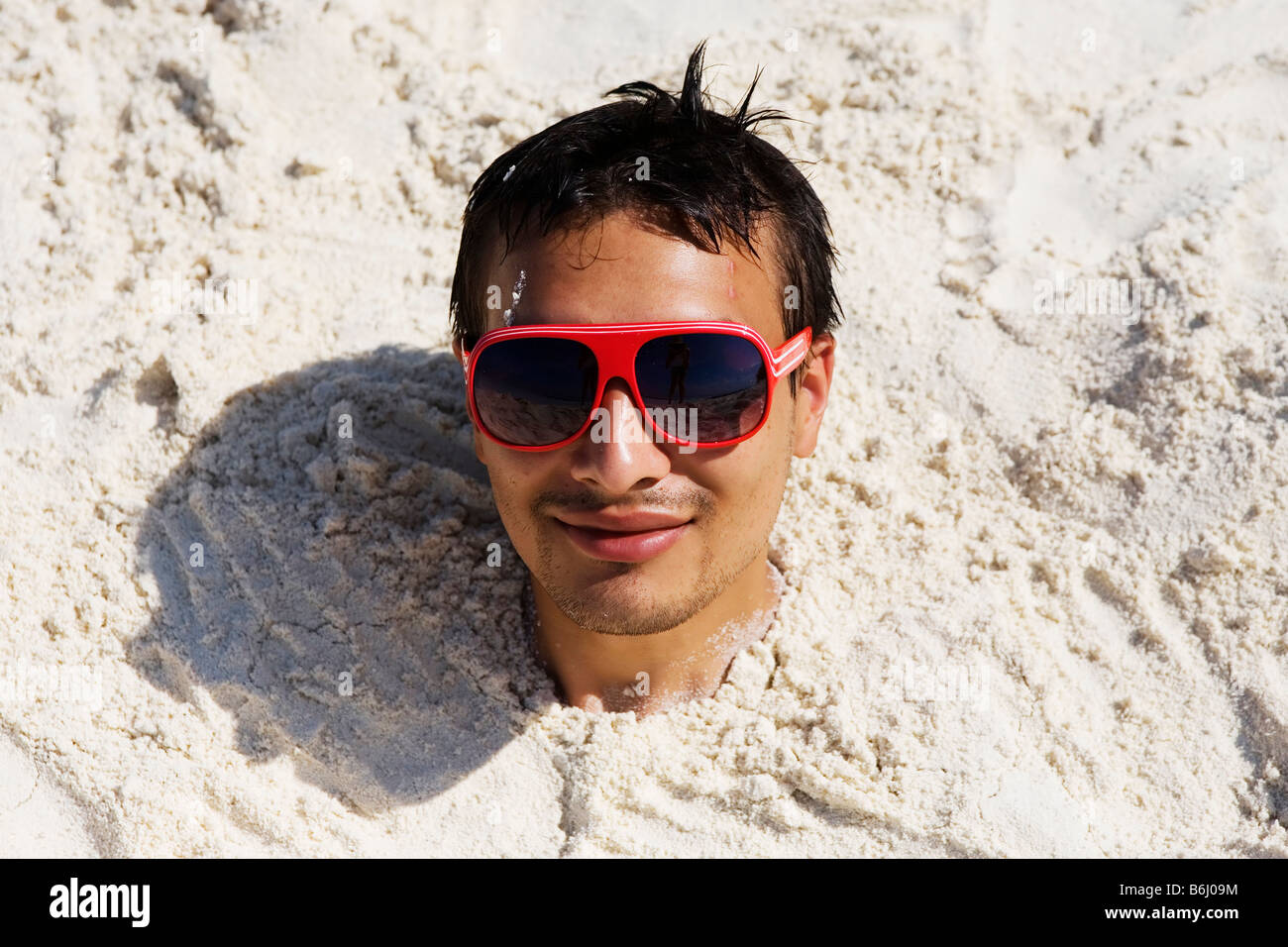 A young man buried up the neck in the sand on a beach in The Maldives Stock Photo