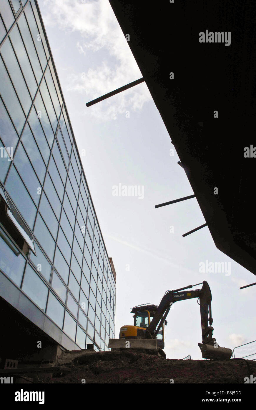 A construction machine pictured between two buildings against the sky. Stock Photo