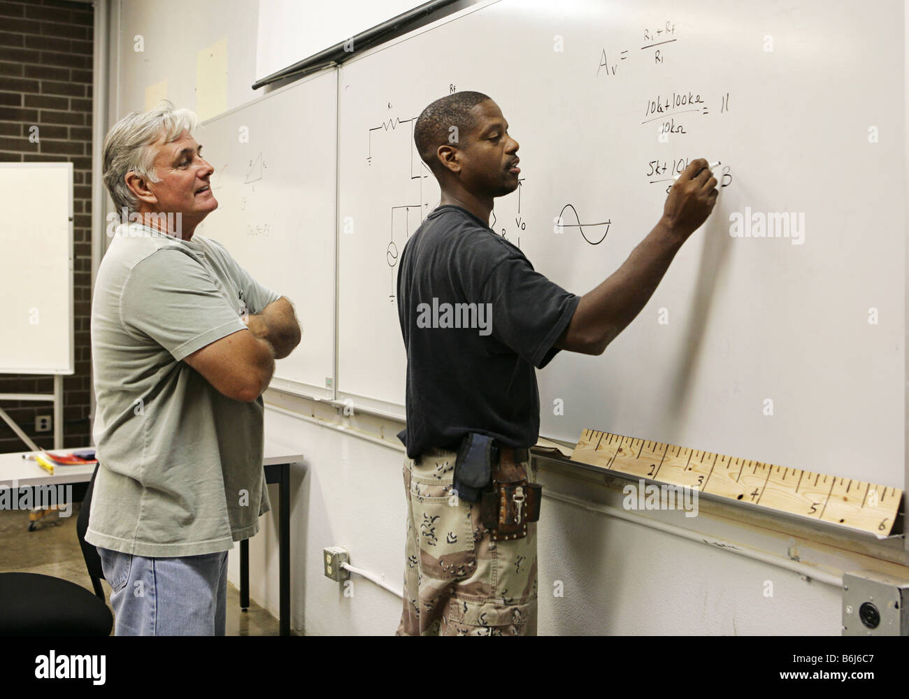 A vocational education teacher looking on as a student does equations on the board Stock Photo