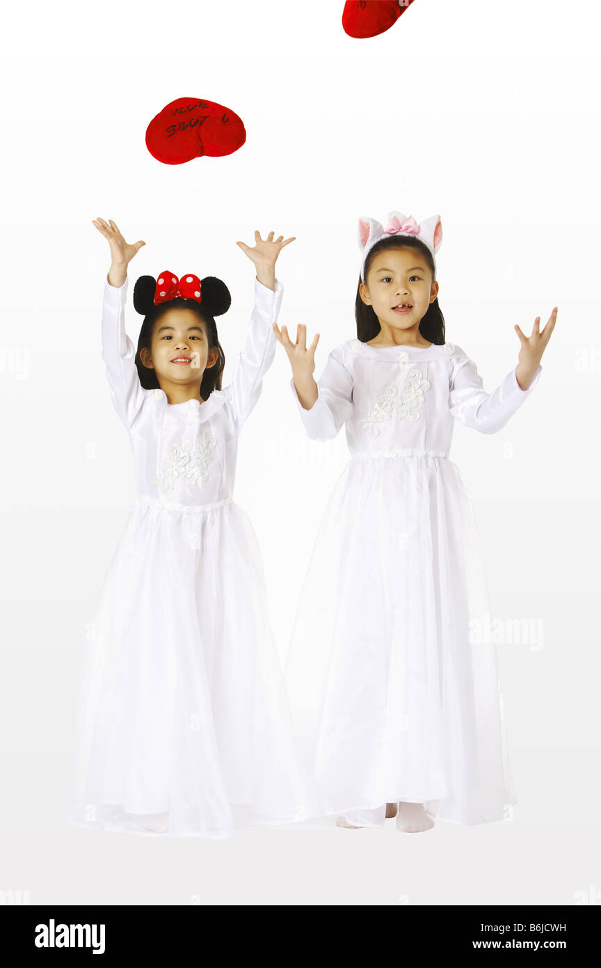 Two young girls wearing white dresses and headbands playing with heart ...