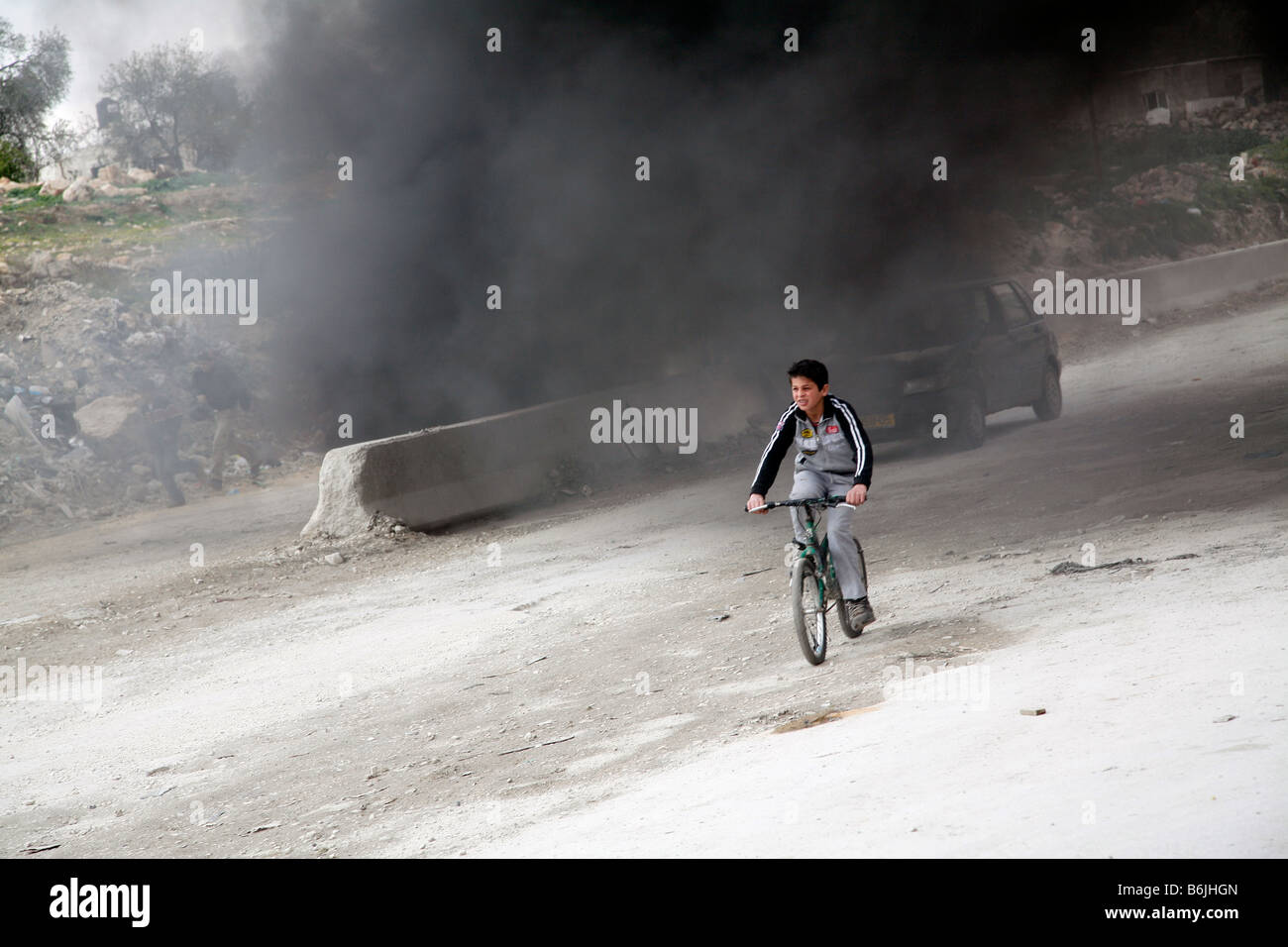 A Palestinian boy cycles through smoke from burning tyres during a protest in the West Bank. Stock Photo