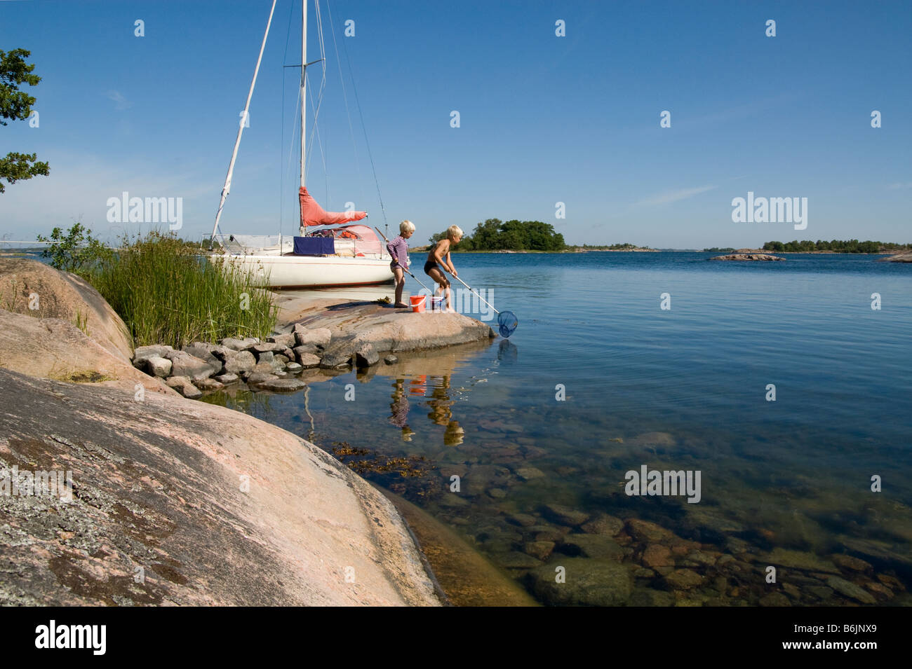young boys fishing with landing net and sailboat in background Stock Photo