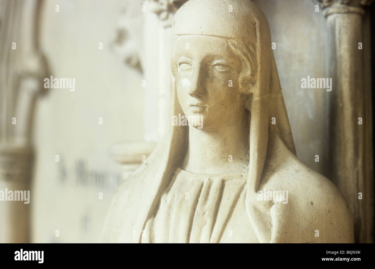 Detail of carved tomb statue of medieval womans head and shoulders with wimple and dress in warm light Stock Photo