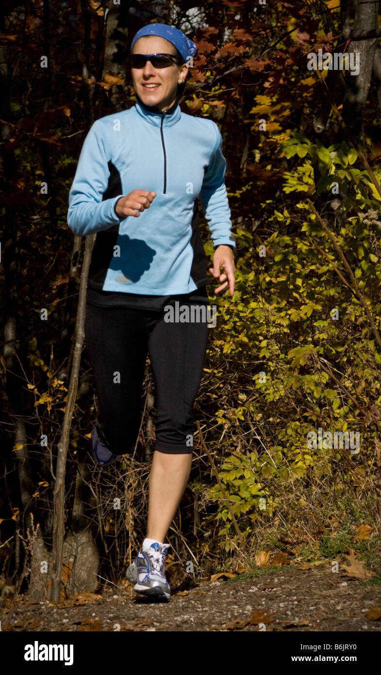 Female trail runner emerges from the forest during her run. Stock Photo