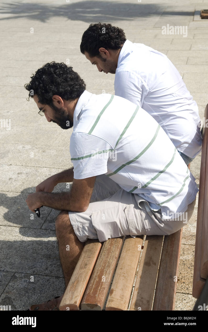 Two men sitting next to each other on a bench outdoors Stock Photo