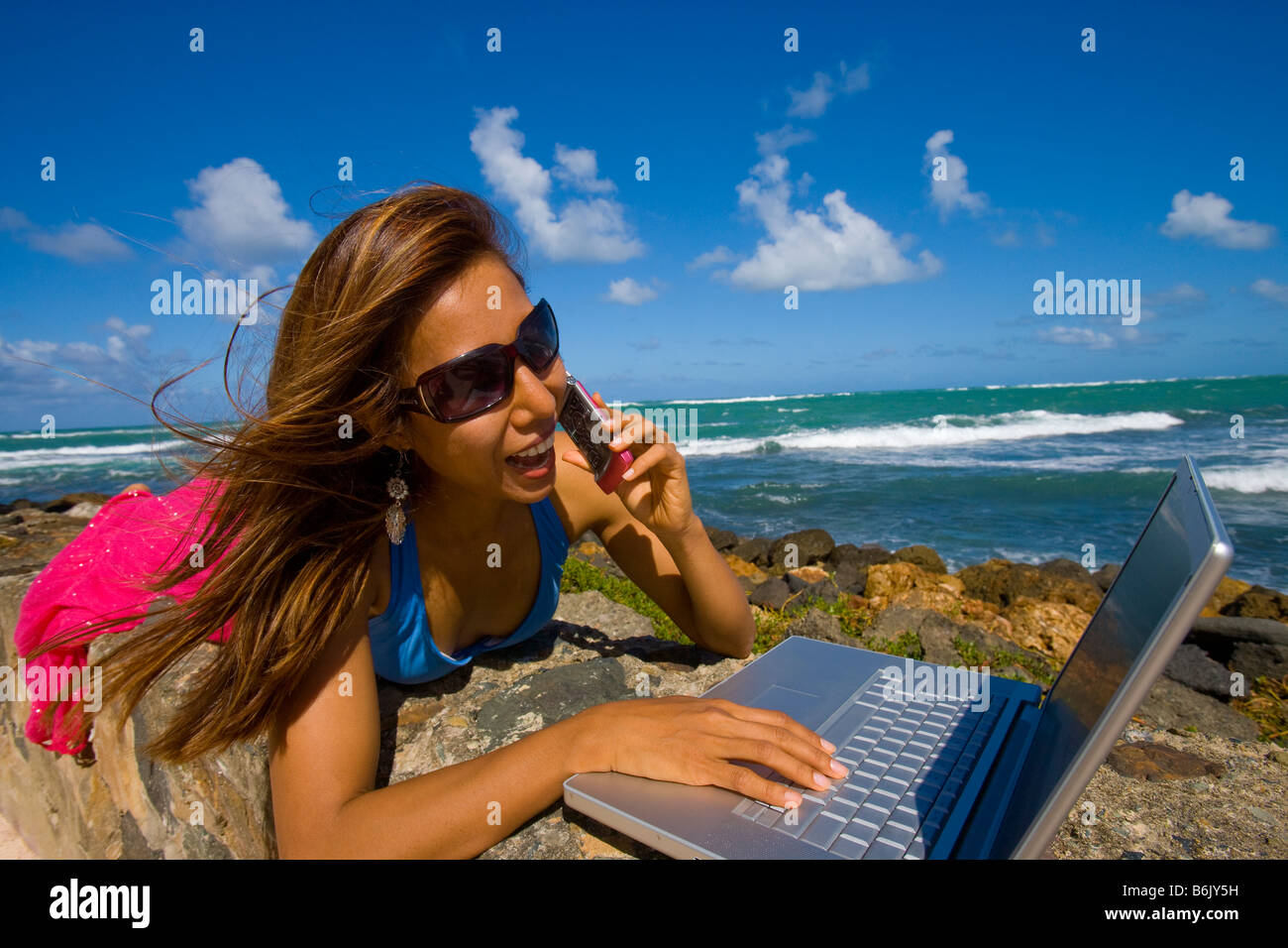 Young Asian woman using a laptop at the beach while she's talking on a