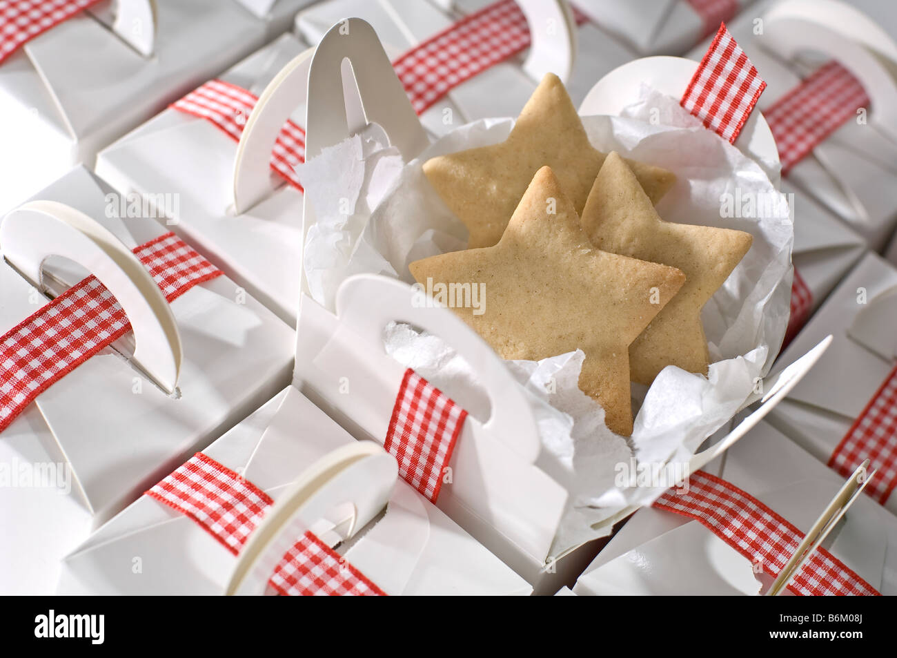 Star shaped cut out biscuits being packed in simple plain white boxes for presents at Christmas. Tied up with red gingham ribbon Stock Photo