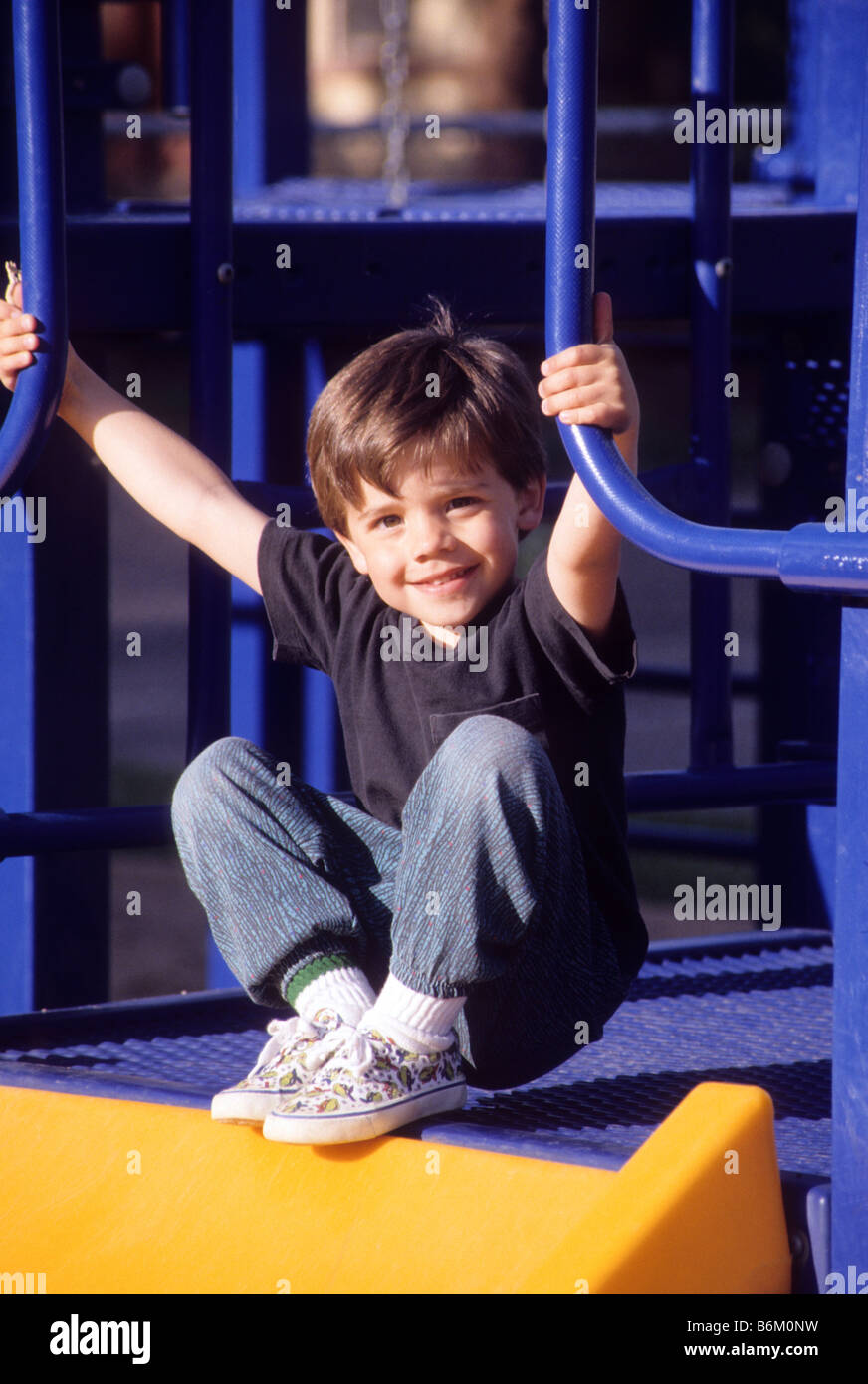Young boy smiles as he prepares to slide down playground equipment in park. Stock Photo