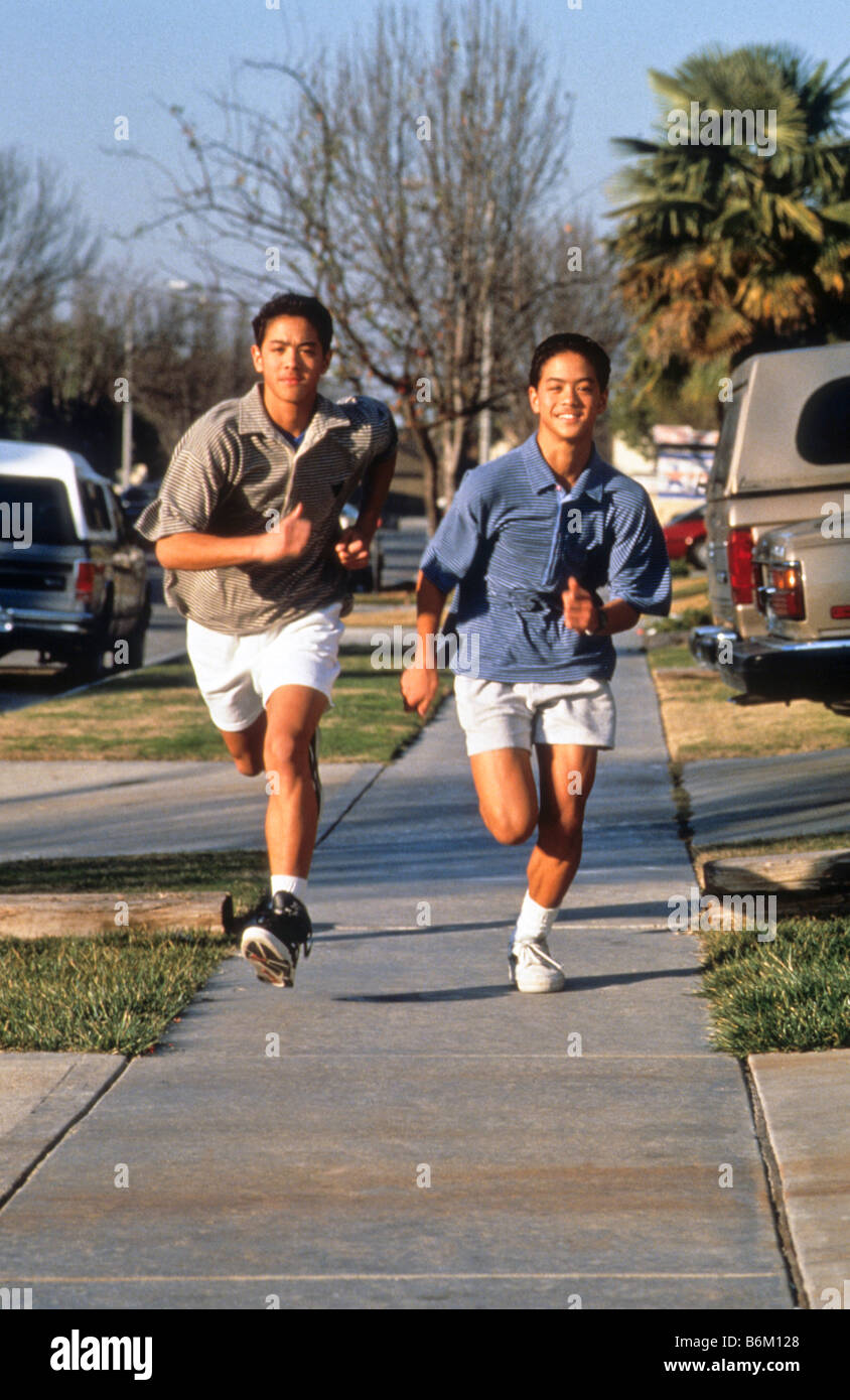 Twin Asian-American boys run down sidewalk in their neighborhood Stock Photo