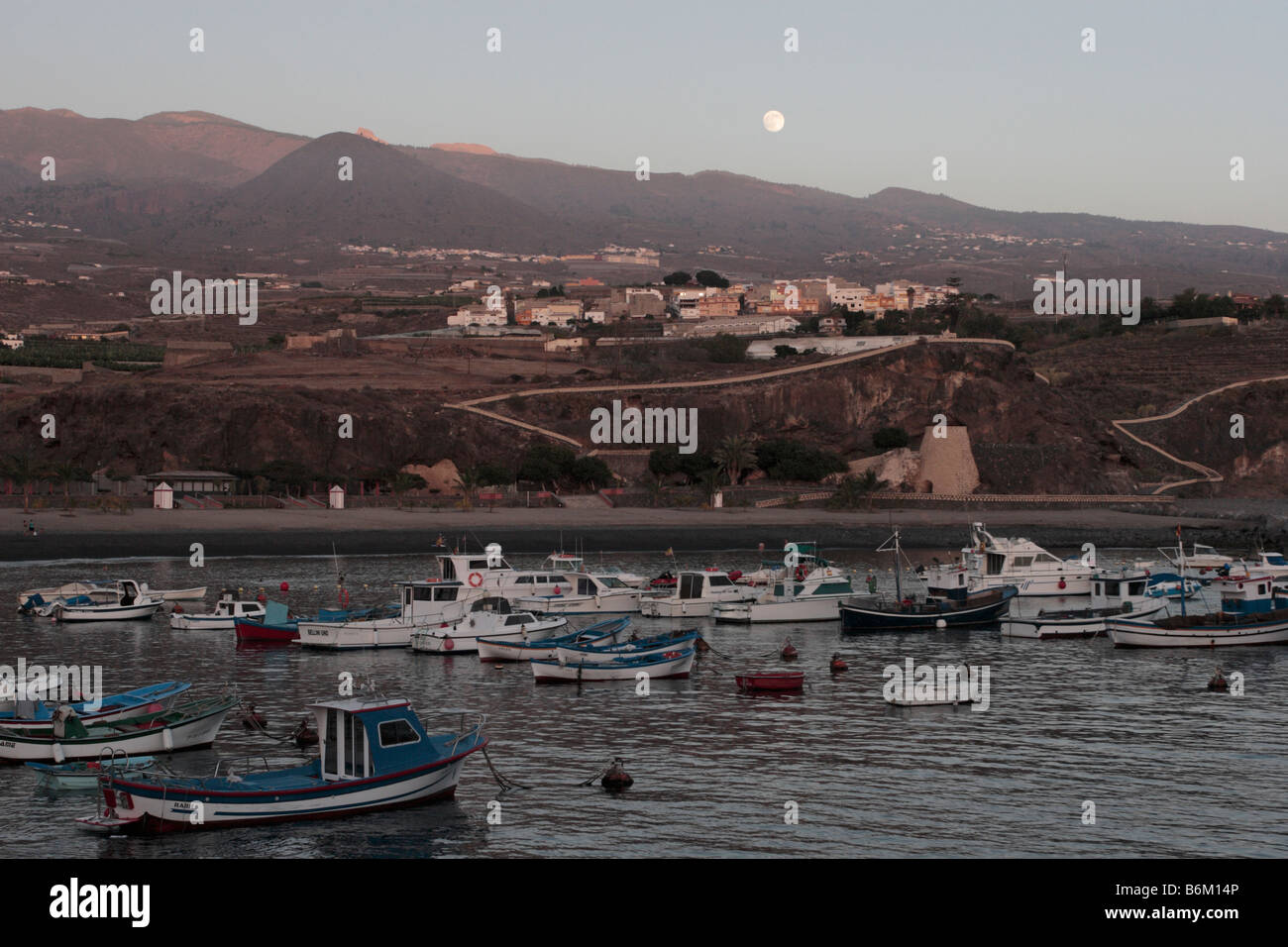 The full moon rising above the harbour of Playa San Juan with the village of Aguadulce behind in Tenerife Canary Islands Spain Stock Photo