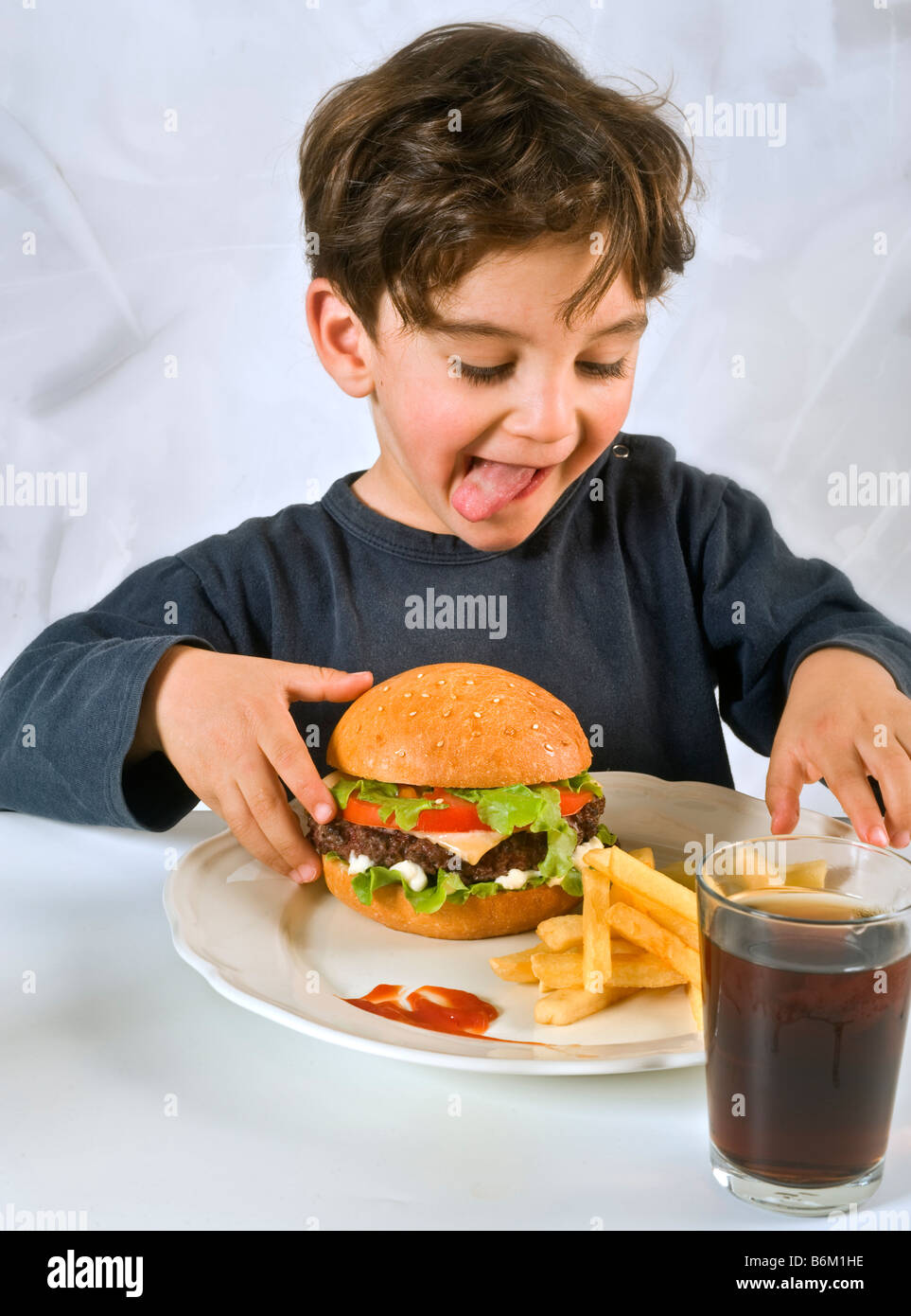 young boy eating chessburger with french fries and coke Stock Photo