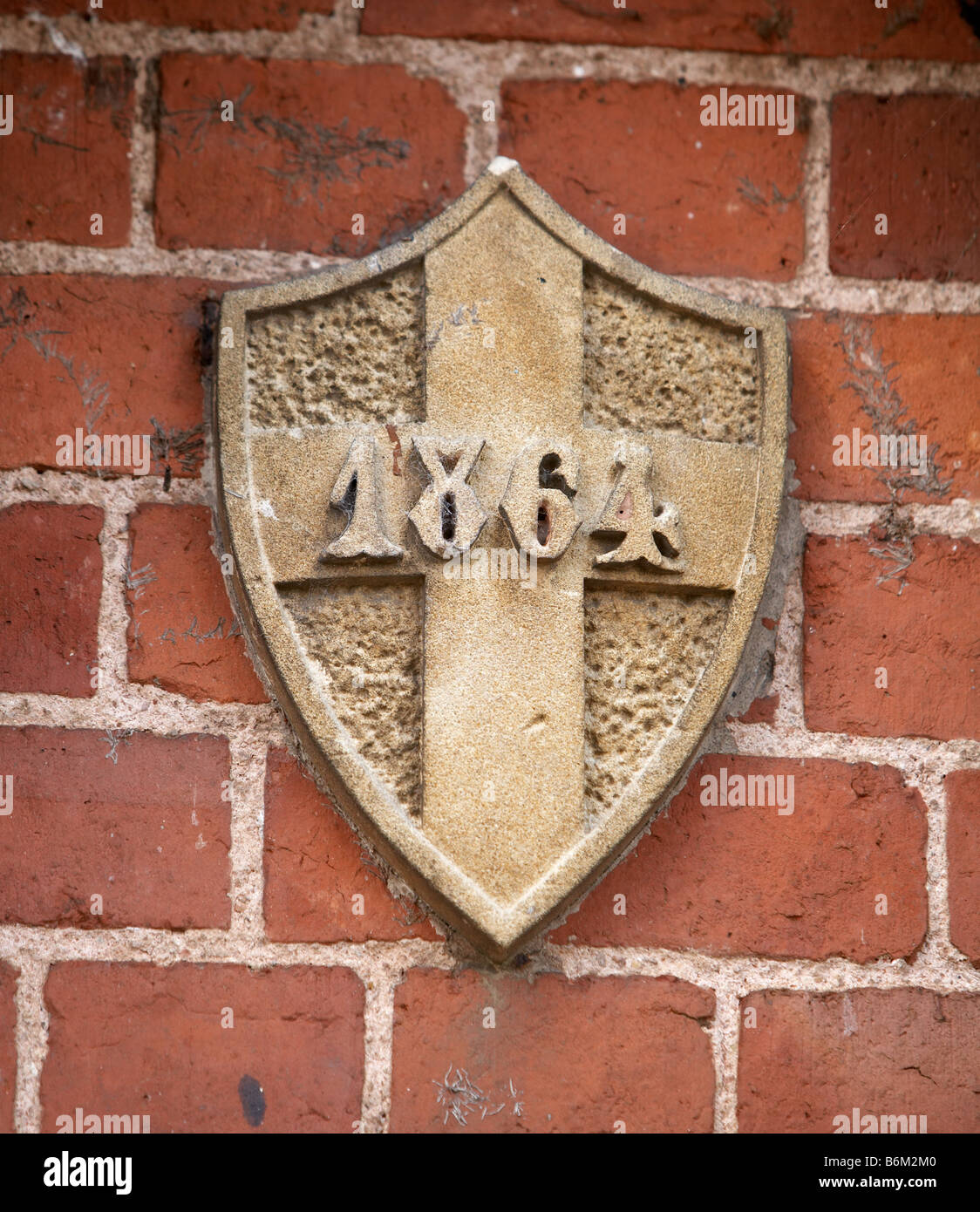 Victorian carved date stone in red brick wall. Shield with cross dated 1864 Stock Photo