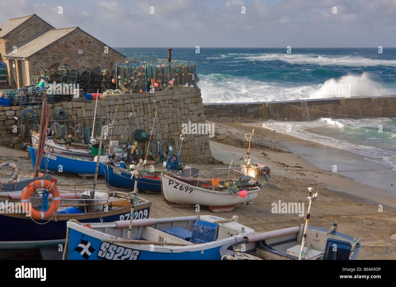 Fishing dinghies drawn up on the beach behind the breakwater at Sennen Cove Cornwall Stock Photo