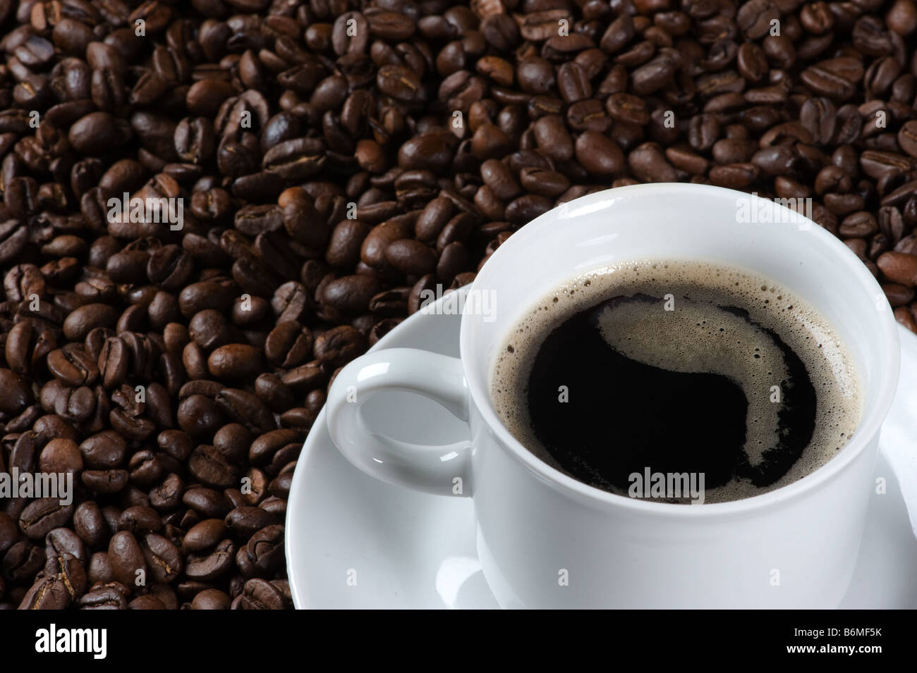 Closeup of a cup of fresh coffee served on a plate covered with freshly roasted coffee beans Stock Photo