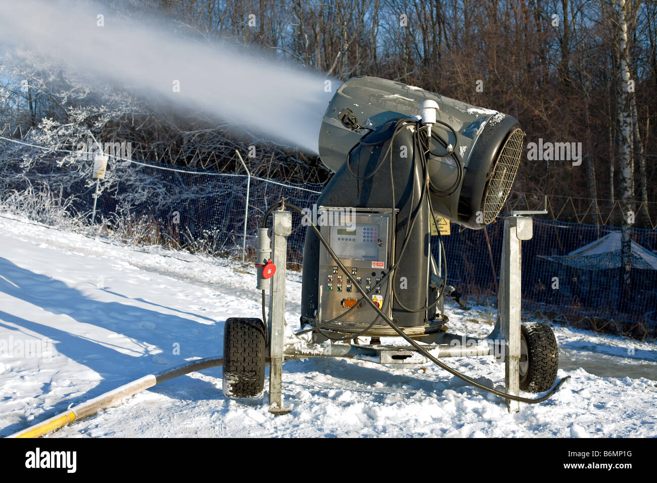 Artificial snow making machine in the Alps. The green artificial snow gun  is against a deep blue sky Stock Photo