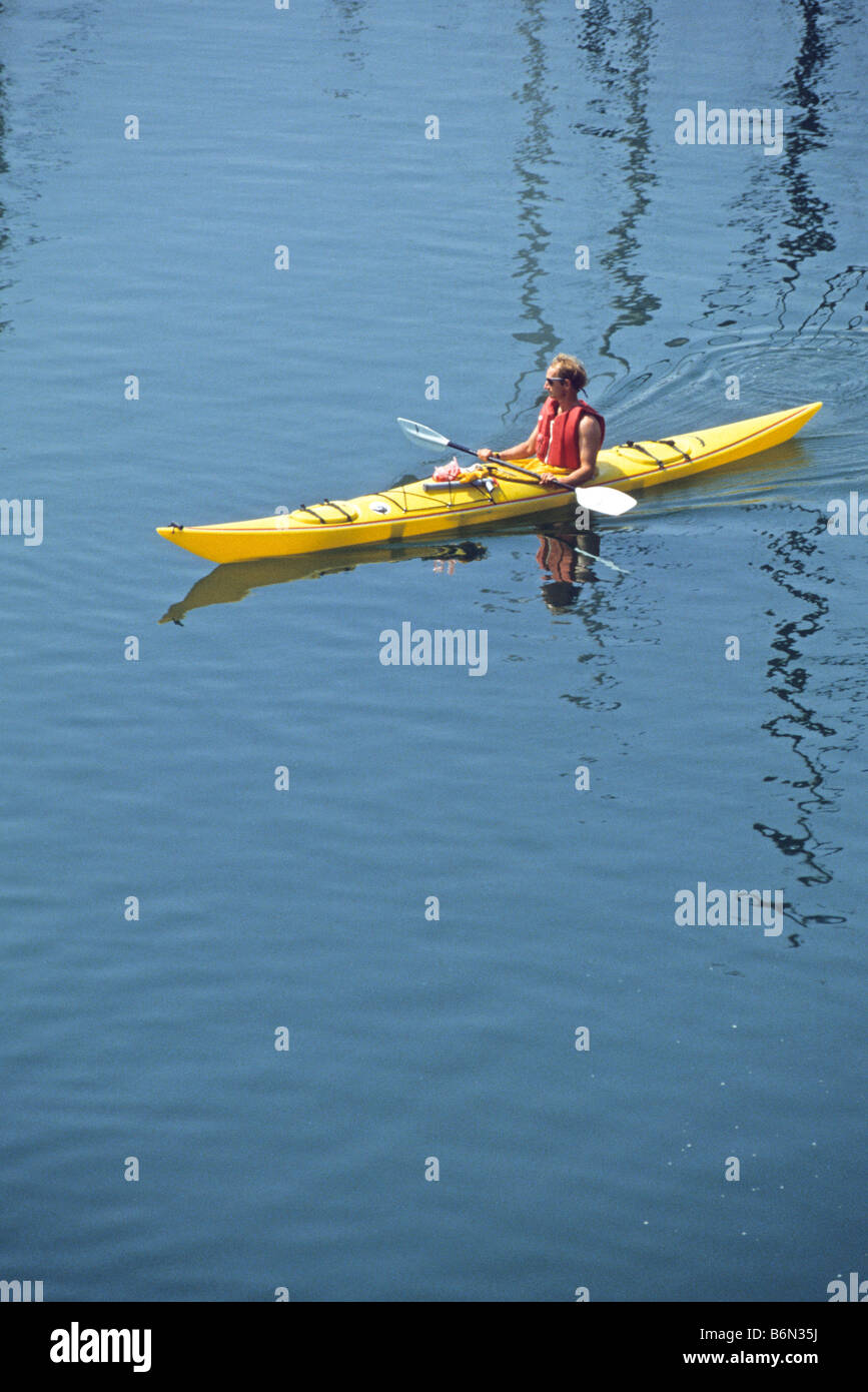 Lone man in kayak coasts through calm waters while resting his paddle. Stock Photo