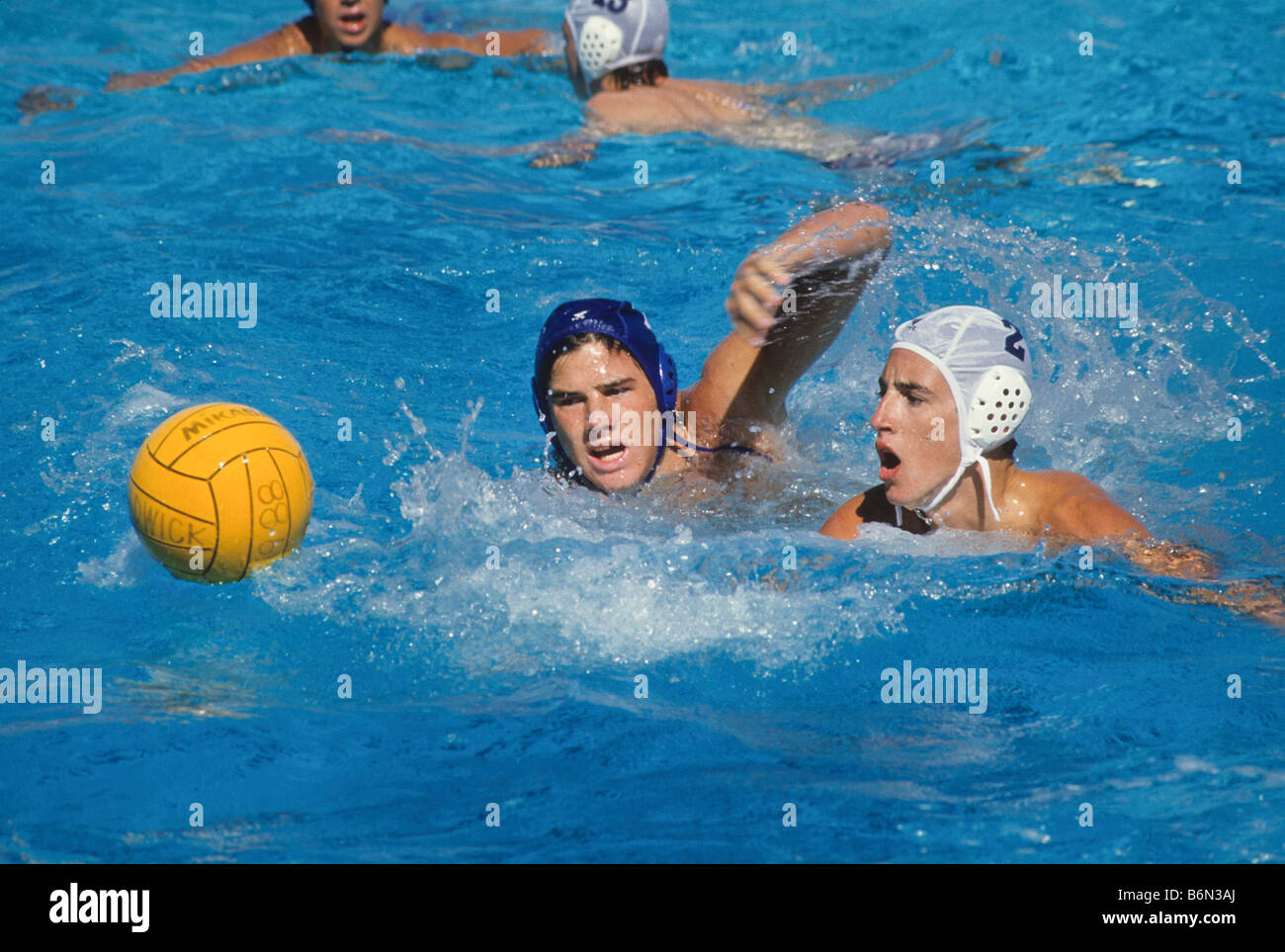 Water polo players chase after loose ball in pool. Stock Photo