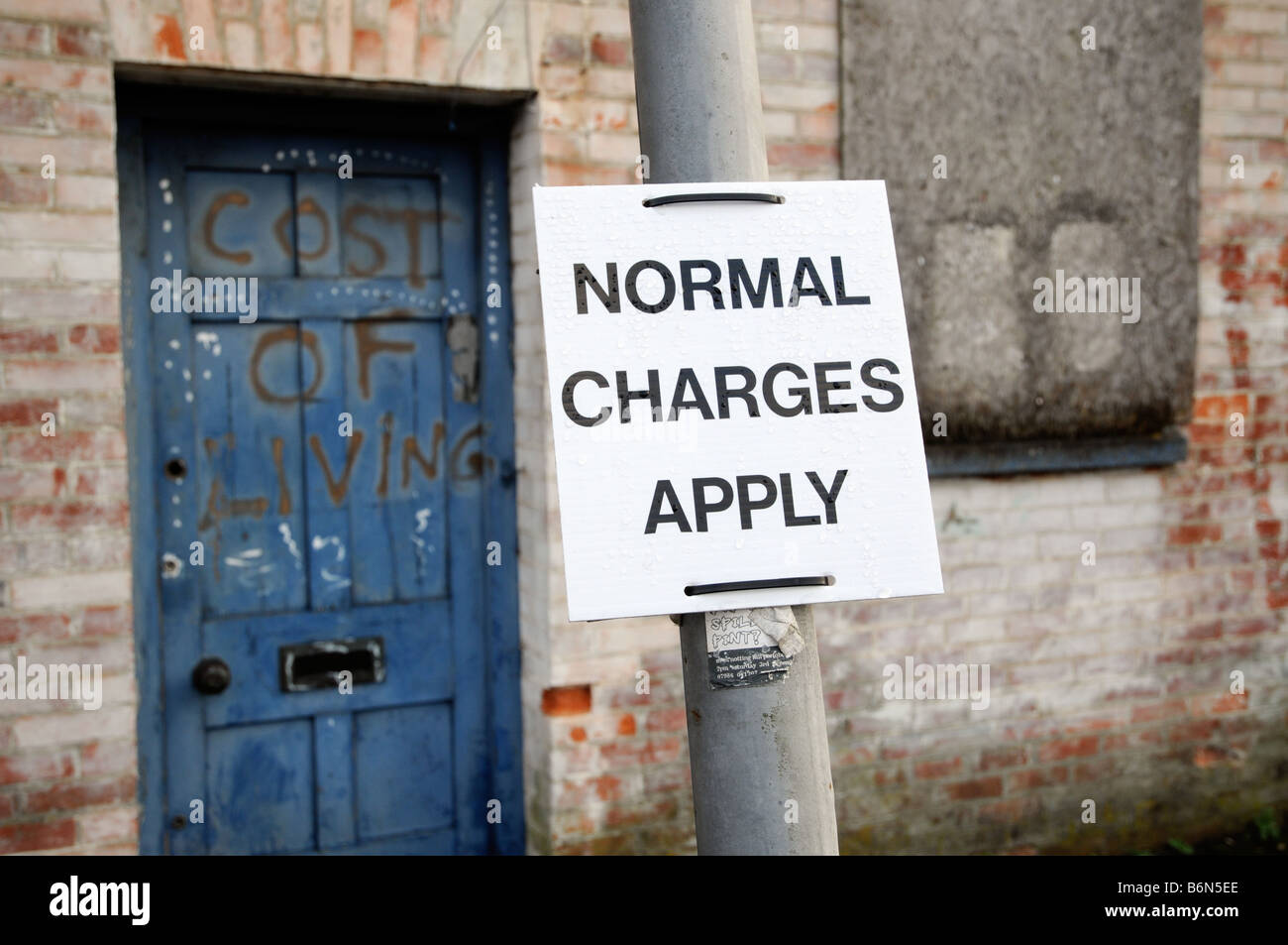 A sign regarding parking charges is attached to a post in front of a door bearing the graffited words 'Cost of living'. Stock Photo