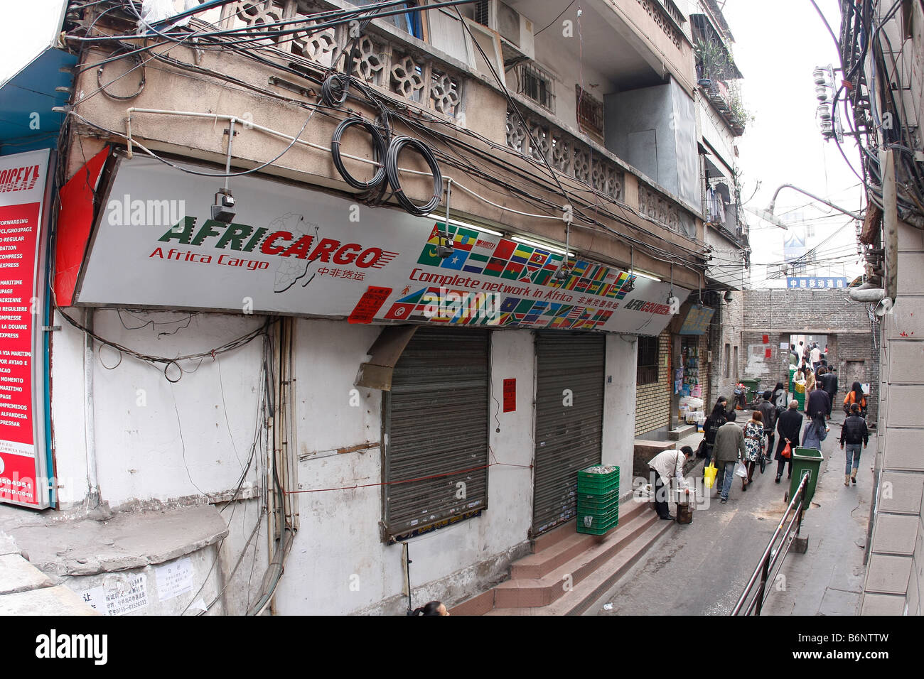 Workers pass through a narrow alleyway shortcut on their way to work under a closed shop sign that specializes in exporting to c Stock Photo