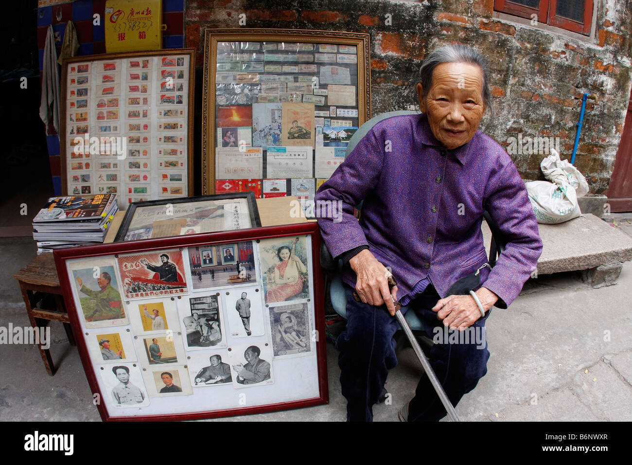 A very nice beautiful and elegant Chinese lady at 93 years old sits in front of her book store in Guangzhou with Mao propaganda. Stock Photo