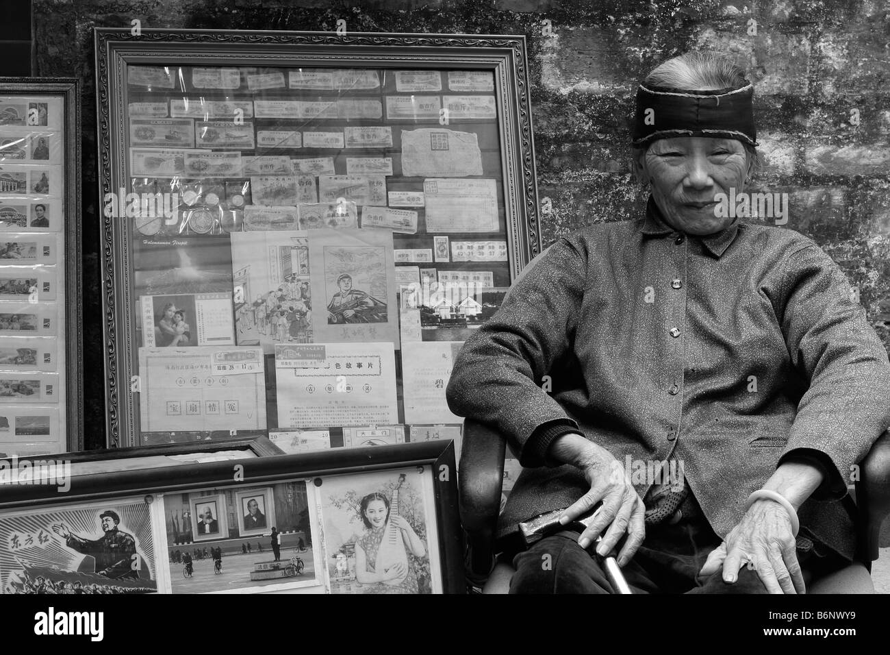 A very nice beautiful and elegant Chinese lady at 93 years old sits in front of her book store in Guangzhou with Mao propaganda. Stock Photo