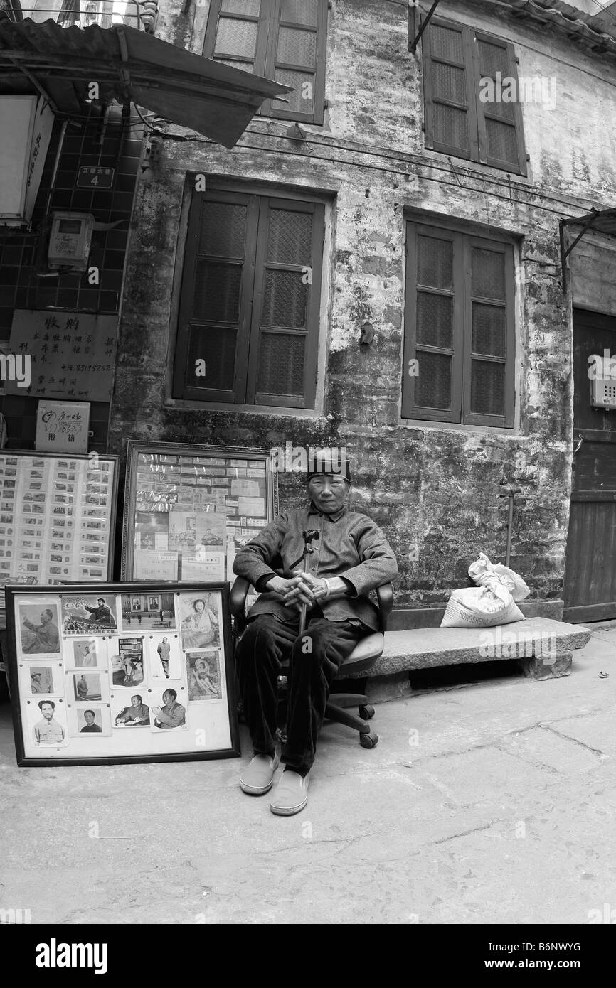 A very nice beautiful and elegant Chinese lady at 93 years old sits in front of her book store in Guangzhou with Mao propaganda. Stock Photo