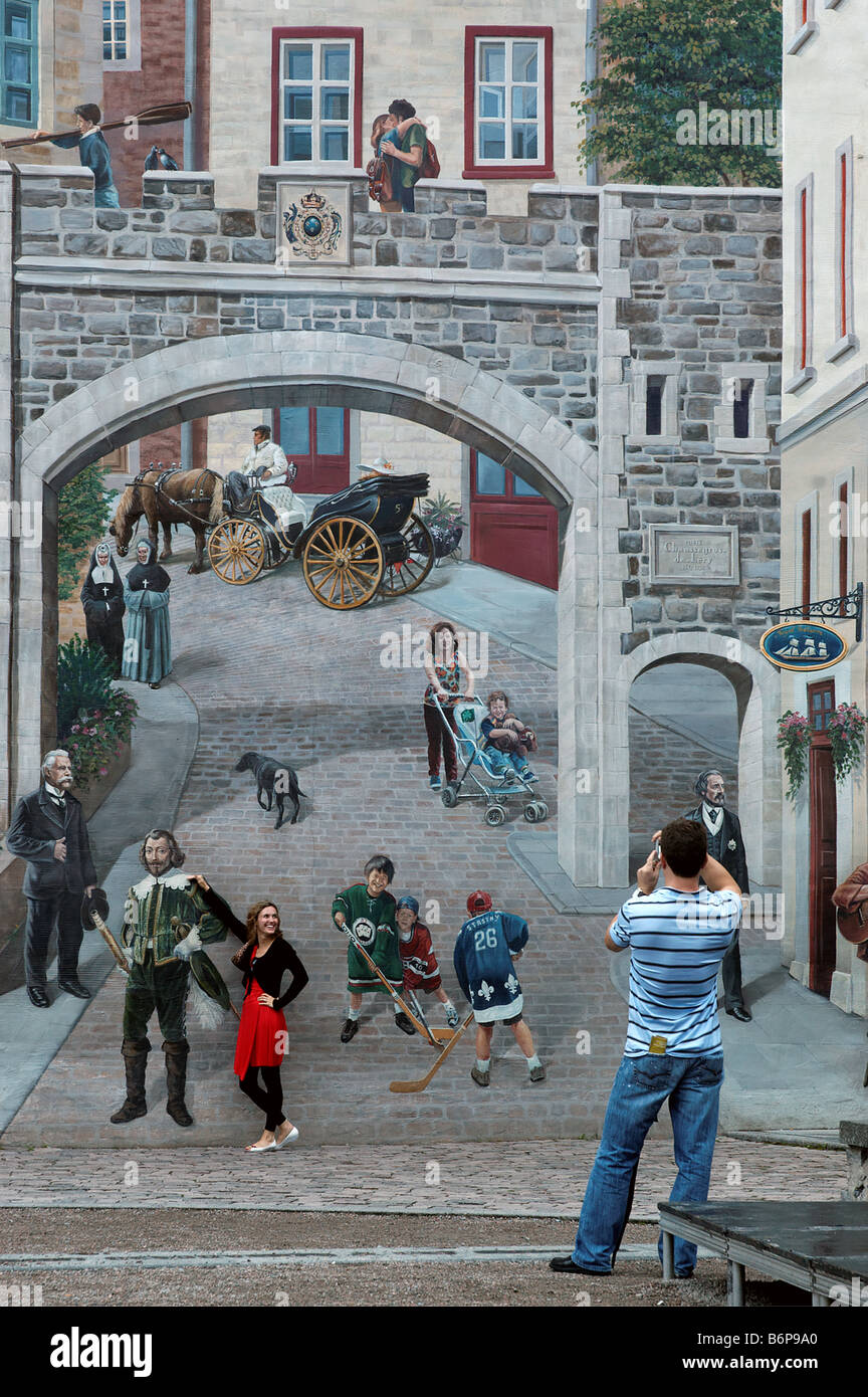 A woman posing for her picture by a figure painted on a wall mural in Quebec City Stock Photo