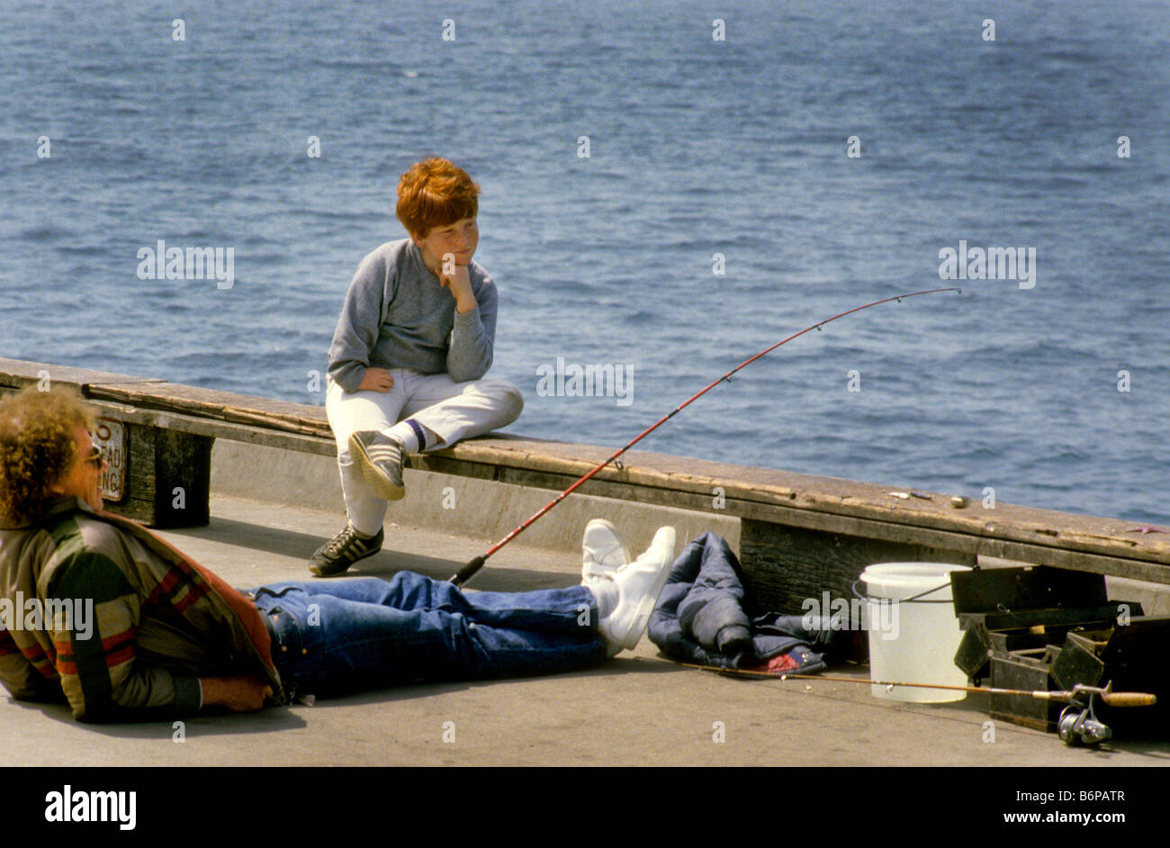 Father and son fish on dock in sunshine. Stock Photo