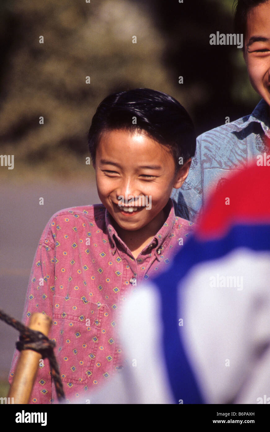 Asian-American boy smiles as he watches friend tie ropes in Boy Scout demonstration camp. Stock Photo