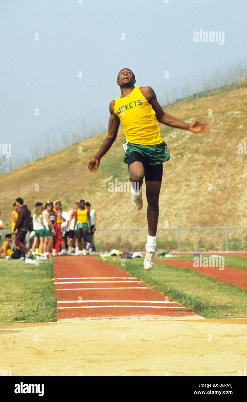 Black teen boy does his best in long jump at high school track meet in